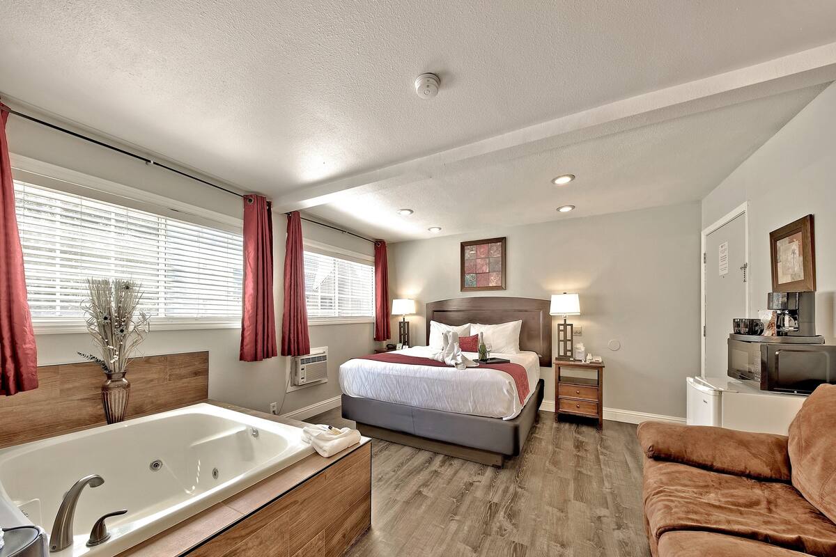 A modern hotel room with a large bed, a separate bathroom with a bathtub, a sofa, and a TV.