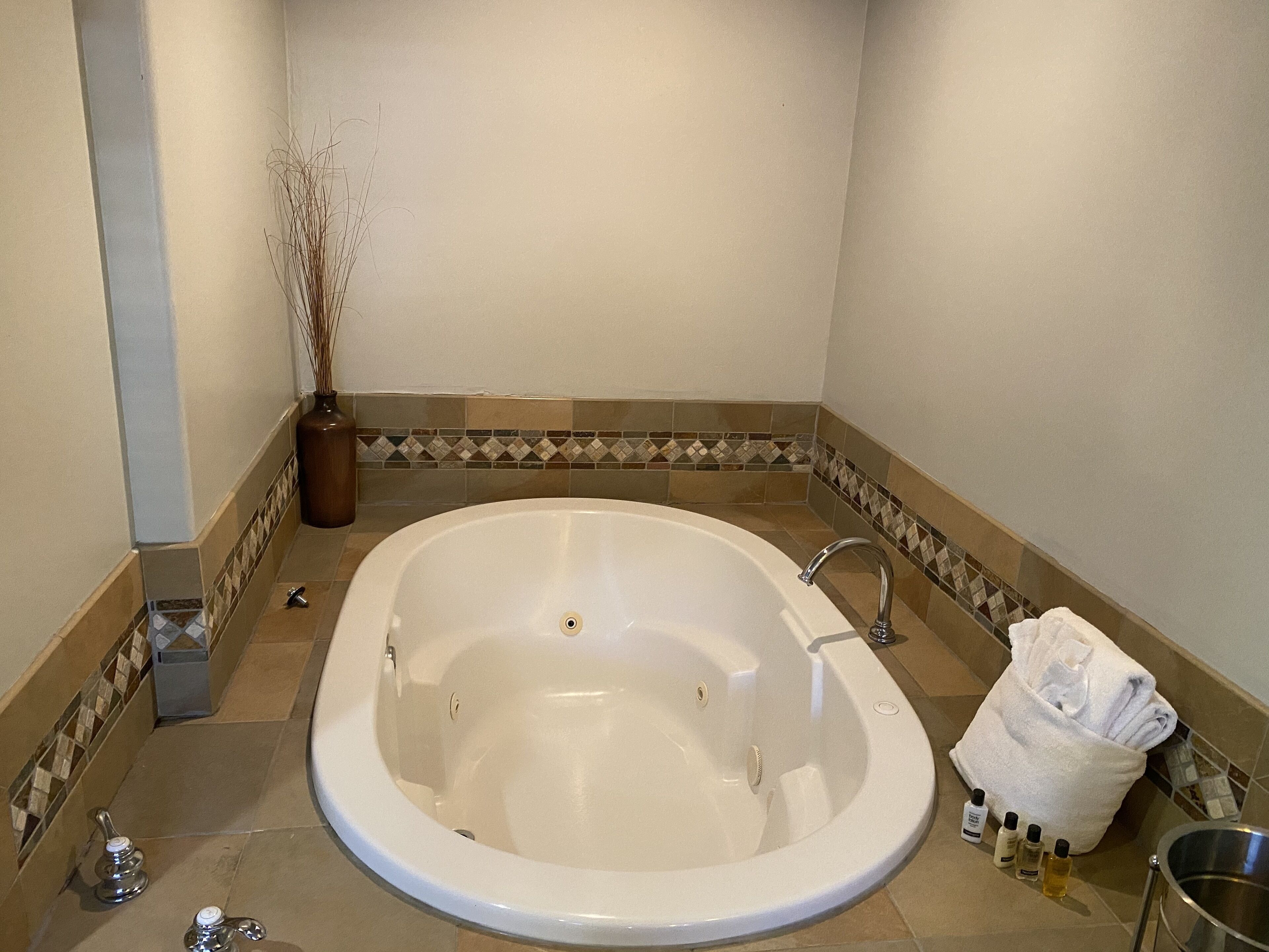 A large, oval-shaped bathtub with a single faucet, surrounded by a tiled floor with a decorative border.