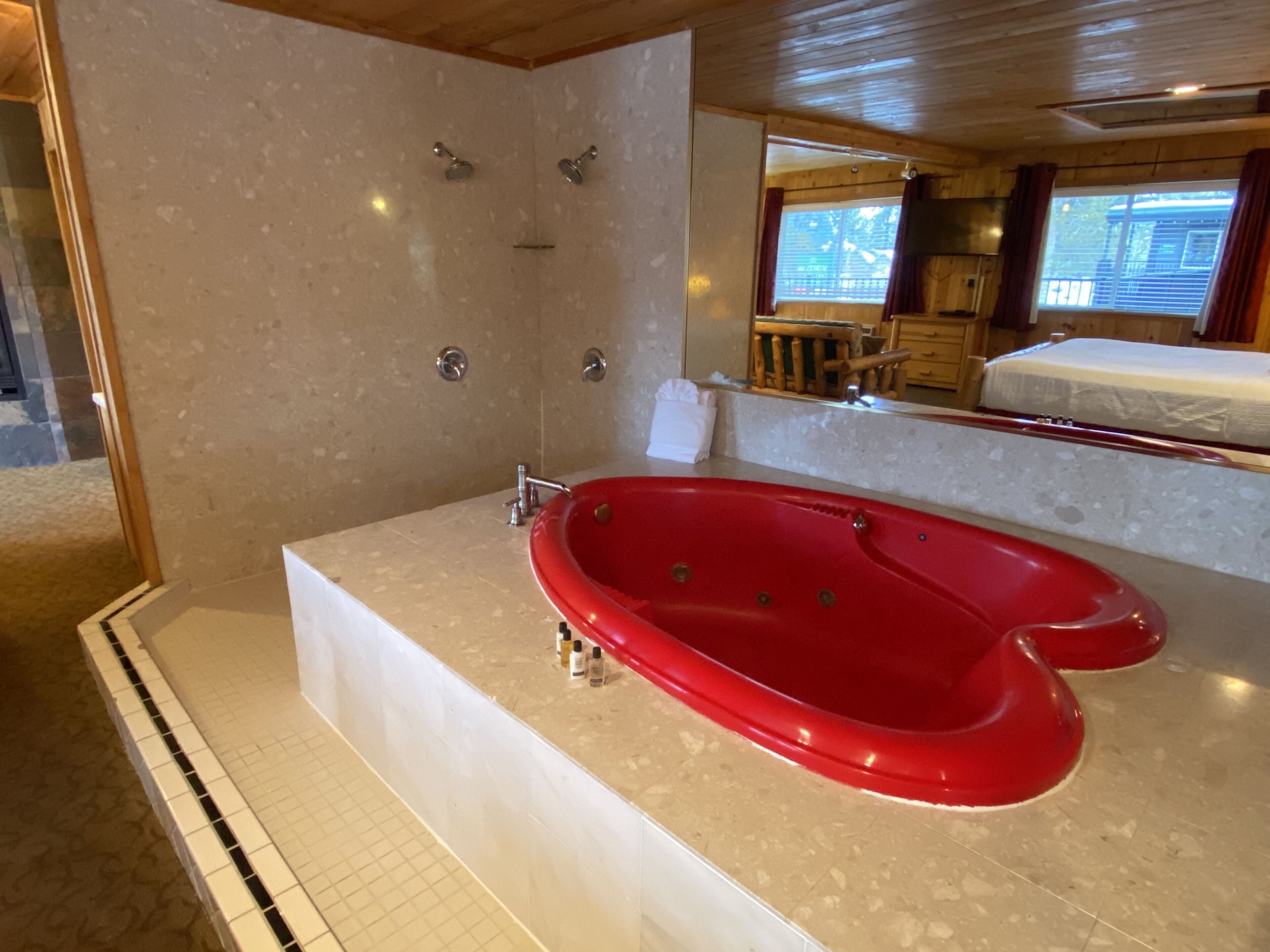 A bathroom with a red bathtub, a shower, and a large mirror.