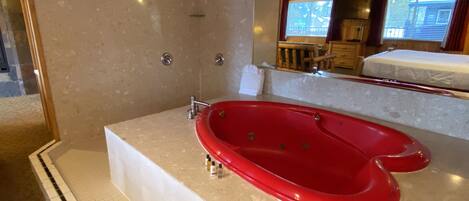 A bathroom with a red bathtub, a shower, and a large mirror.