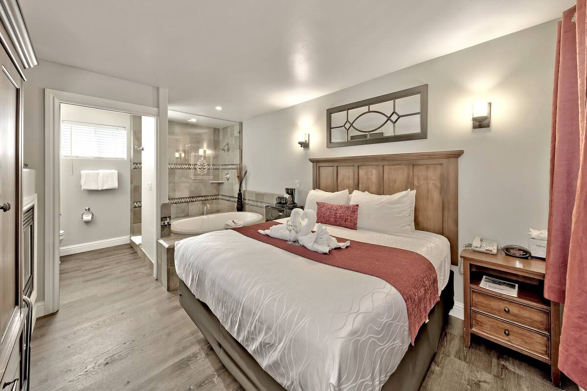 A hotel room with a large bed, a wooden nightstand, a bathroom with a bathtub, and a shower.