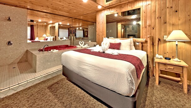 Une chambre à coucher de style cabane en bois, avec un grand lit, une baignoire rouge, un miroir et un bureau en bois avec une lampe.