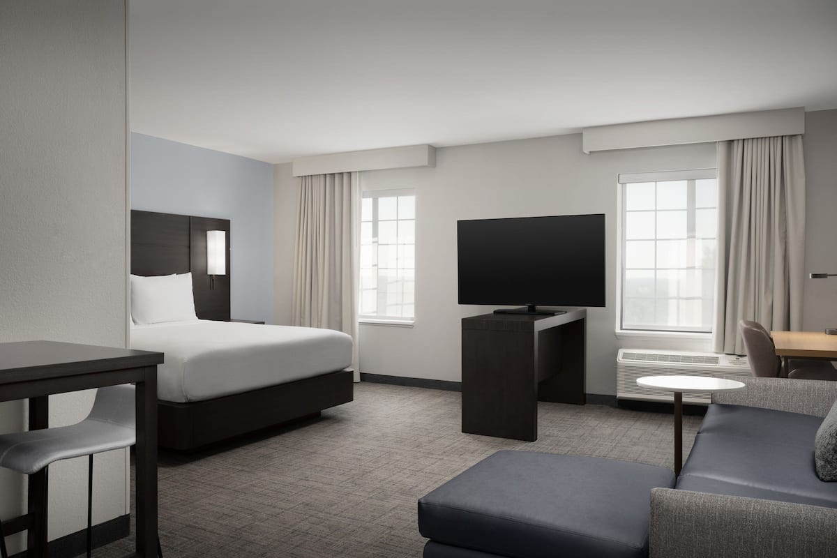 A modern hotel room with a bed, a TV, a sofa, and a desk.