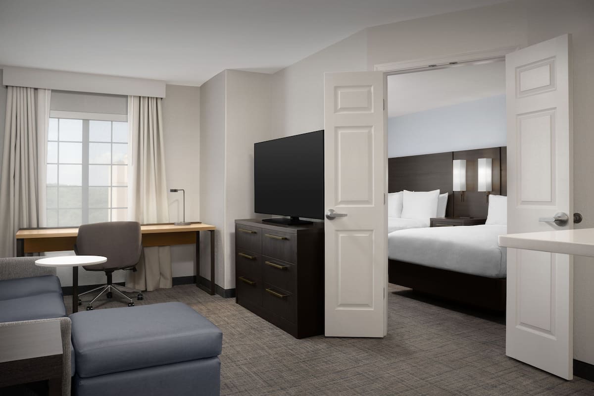 A hotel room with a bed, a desk with a chair, a television, and a wardrobe.