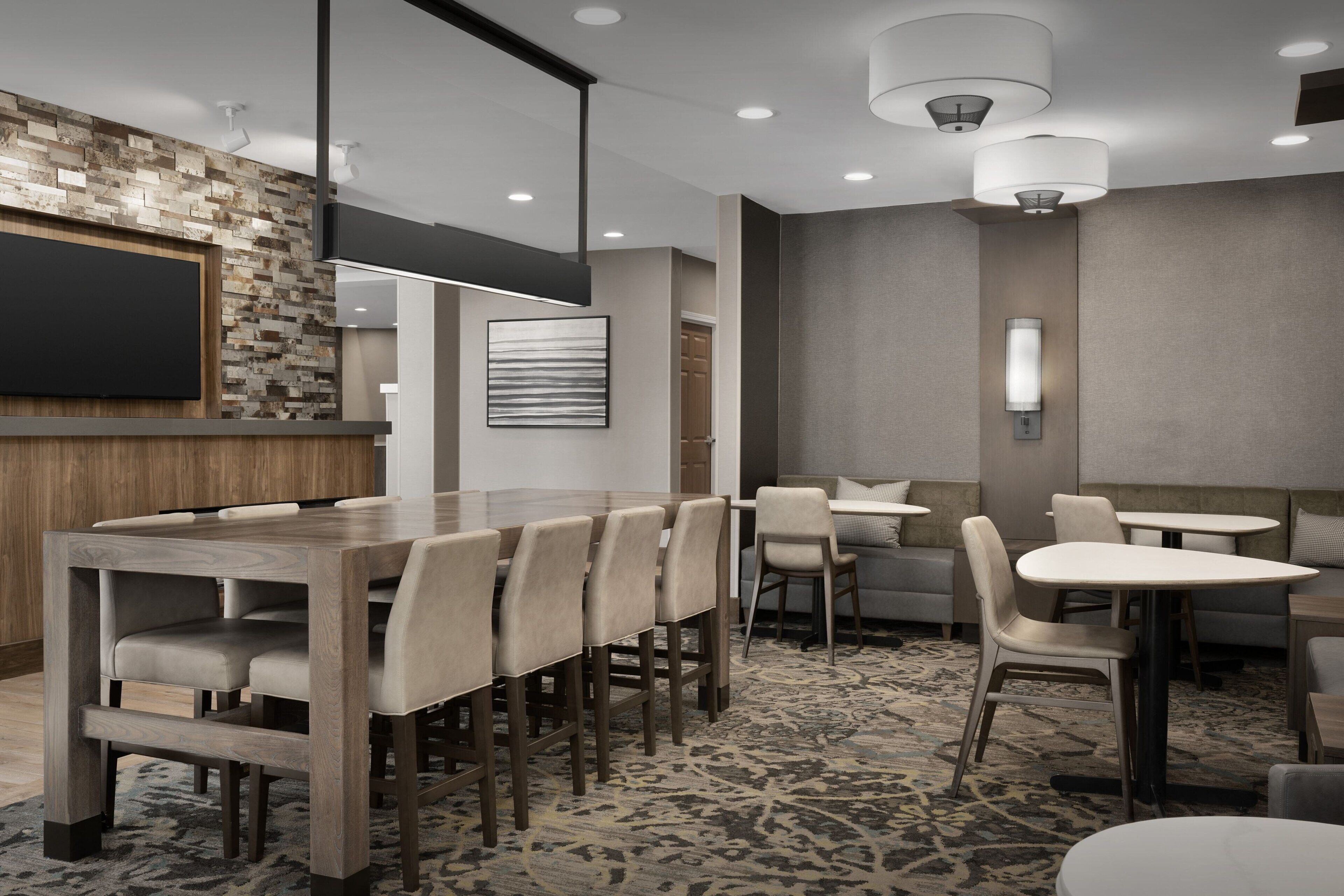 A modern hotel lobby with a wooden reception desk, multiple seating areas, and a patterned carpet.