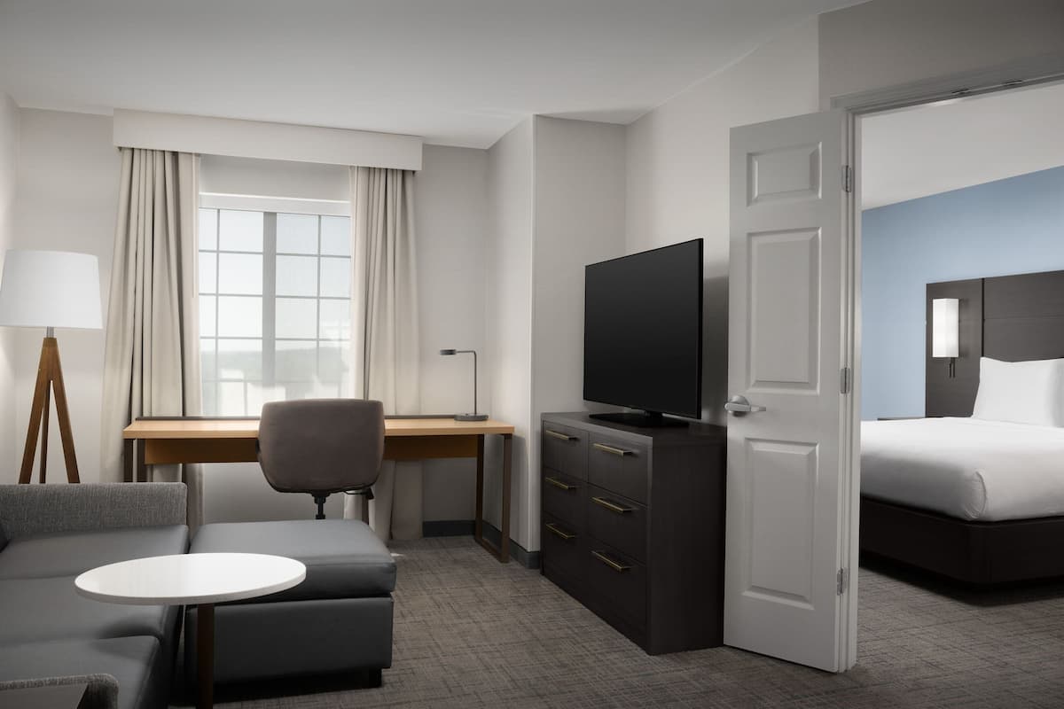A hotel room with a bed, a desk with a chair, a television, a sofa, and a small table.