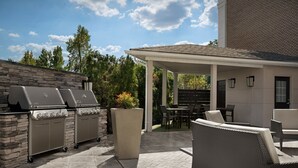Eine Terrasse im Freien mit einer Steinsäule, einer überdachten Sitzgruppe und einem Grill.