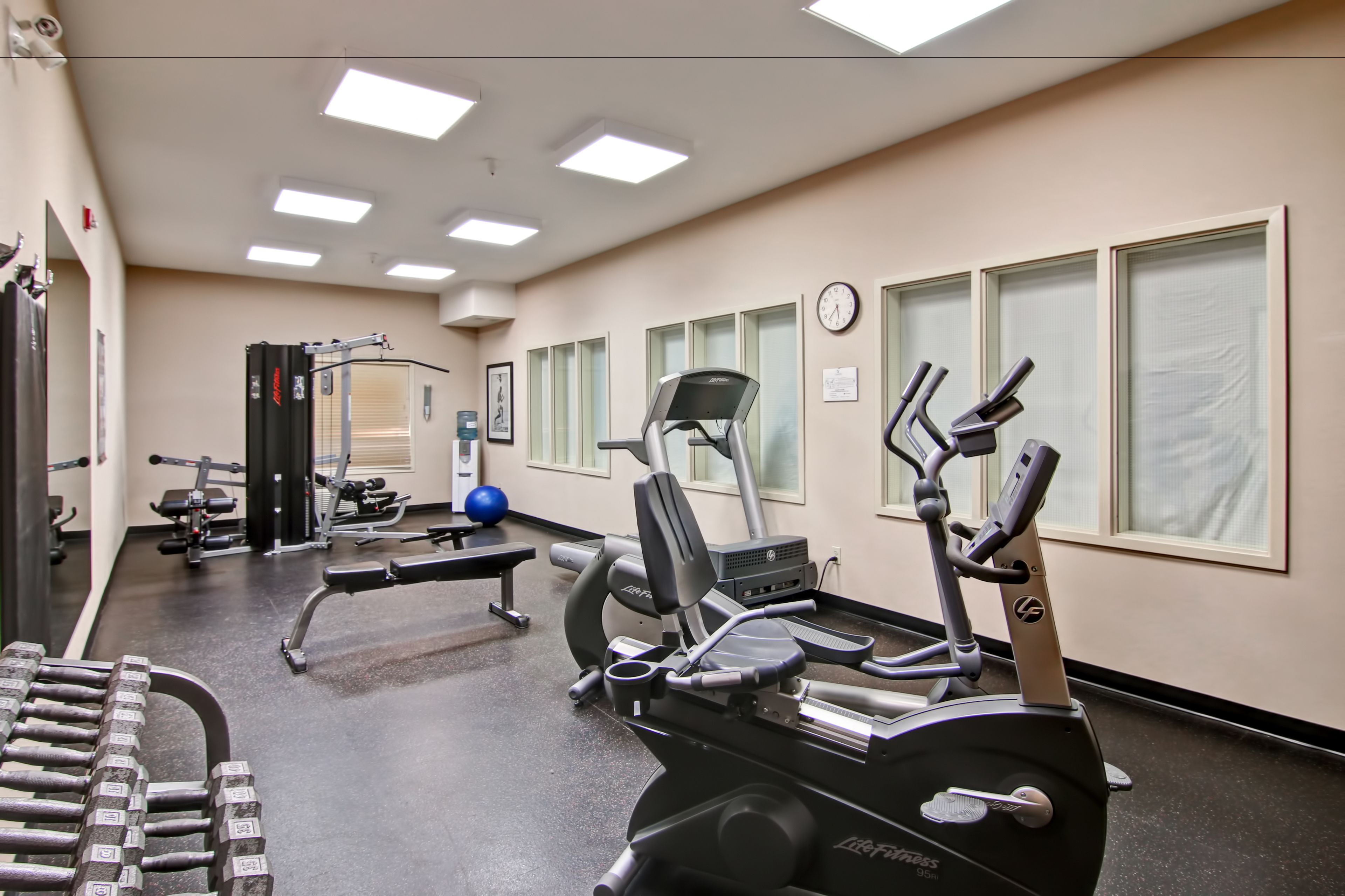 Un gimnasio con equipo de ejercicio, una banca y un reloj de pared.
