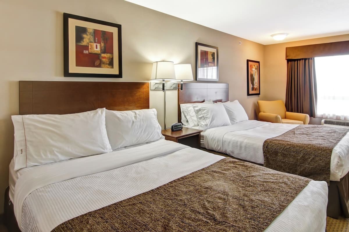 A hotel room with two beds, a nightstand with a lamp, a chair, and artwork on the walls.