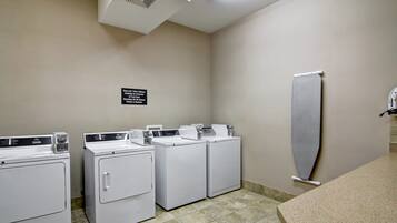 A laundry area with three stacked washers and dryers, a sign indicating fabric care instructions, and a towel rack on the wall.