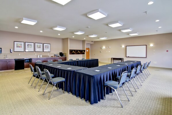 Un salón de conferencias con una larga mesa, sillas, una pantalla de proyector y una zona de cocina.