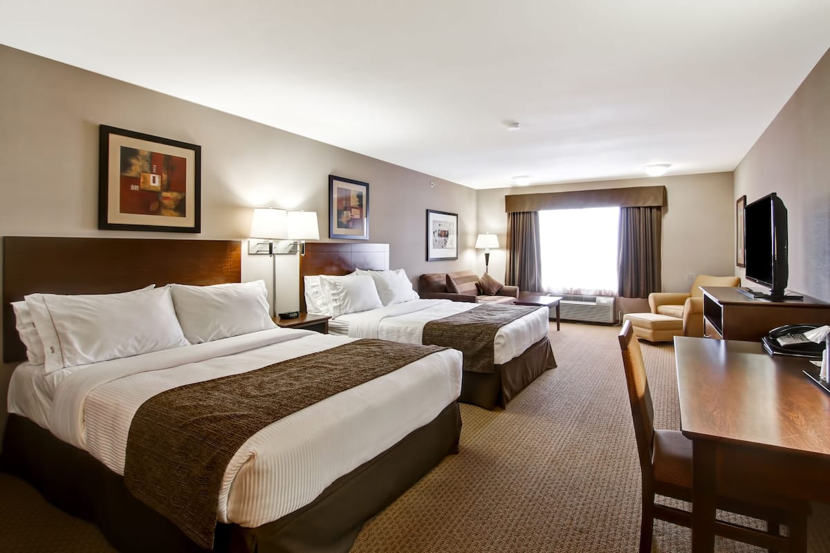 A hotel room with two beds, a desk, a TV, and a large window.