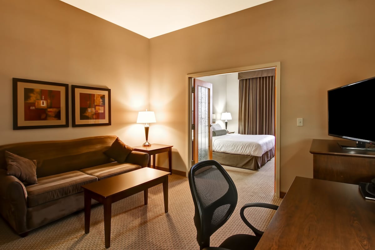 A hotel room with a sofa, a desk, a chair, a television, and a bed.