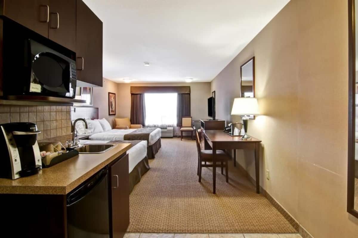 A compact hotel room with a kitchenette, a bed, a desk, and a chair.