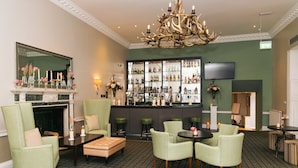A bar area with green upholstered chairs, a fireplace, and a bar stocked with various bottles. - Highfield Park (Hook)