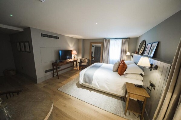 A hotel room with a bed, a desk, a chair, a TV, and a lamp.