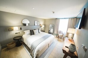 Ein modernes Hotelzimmer mit einem großen Bett, Nachttischen, einem Sessel, einem Schreibtisch und einem Fernseher.
