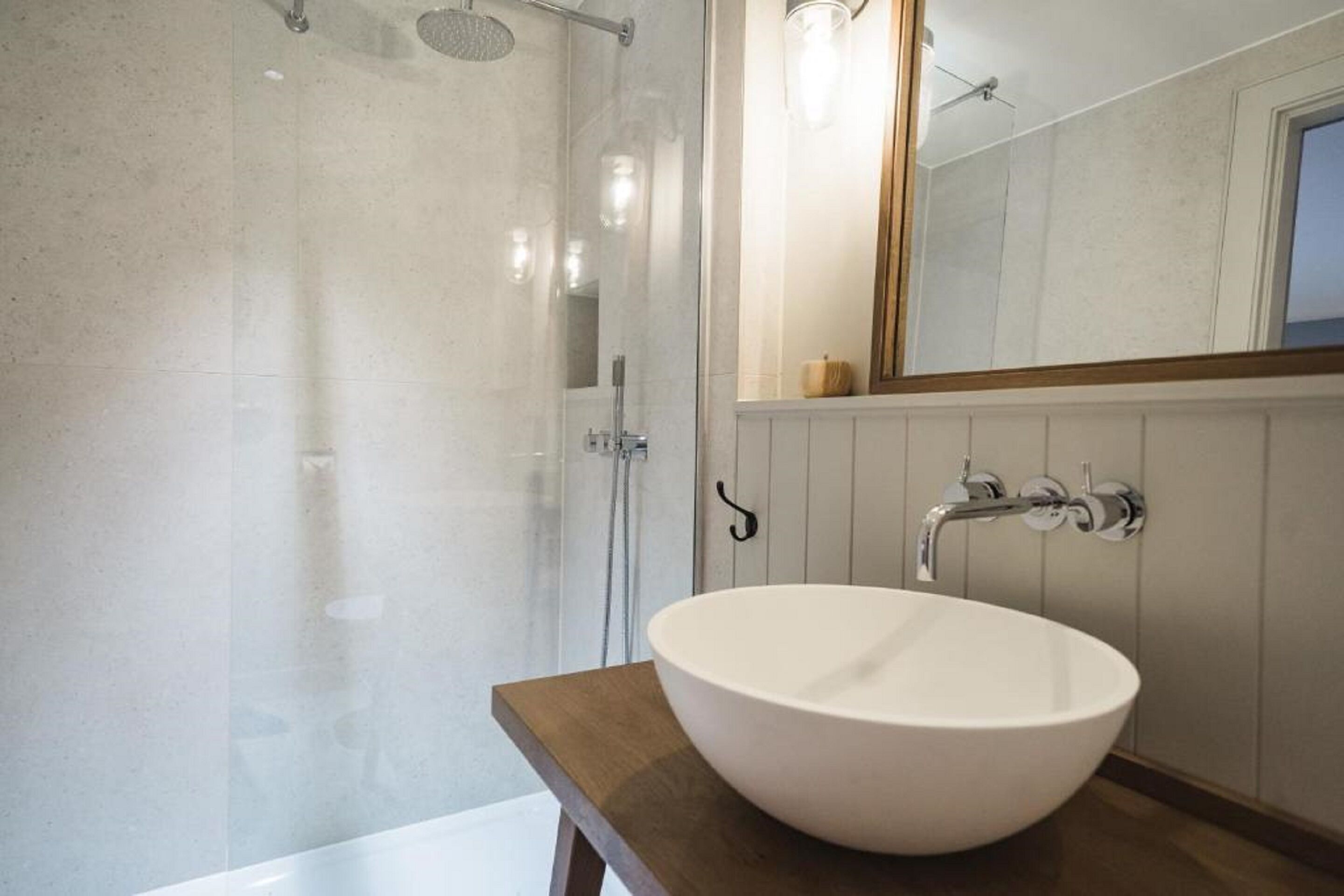 A modern bathroom with a large white sink, a glass-enclosed shower, and a wooden vanity.