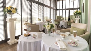A dining area with round tables set for tea service, featuring floral decorations and a view through large windows. - Highfield Park (Hook)