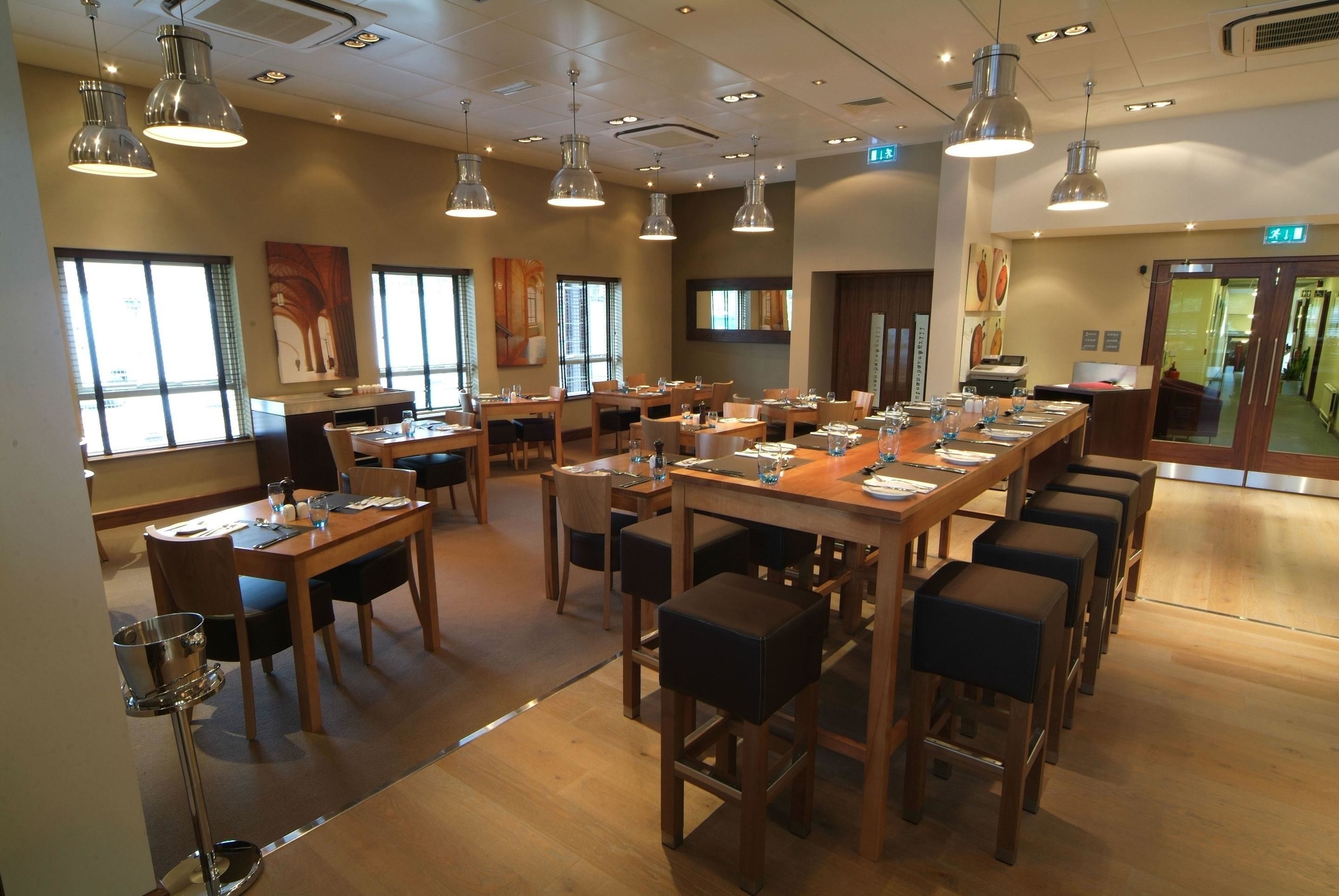 A spacious dining area with multiple tables and chairs, large windows, and pendant lighting.