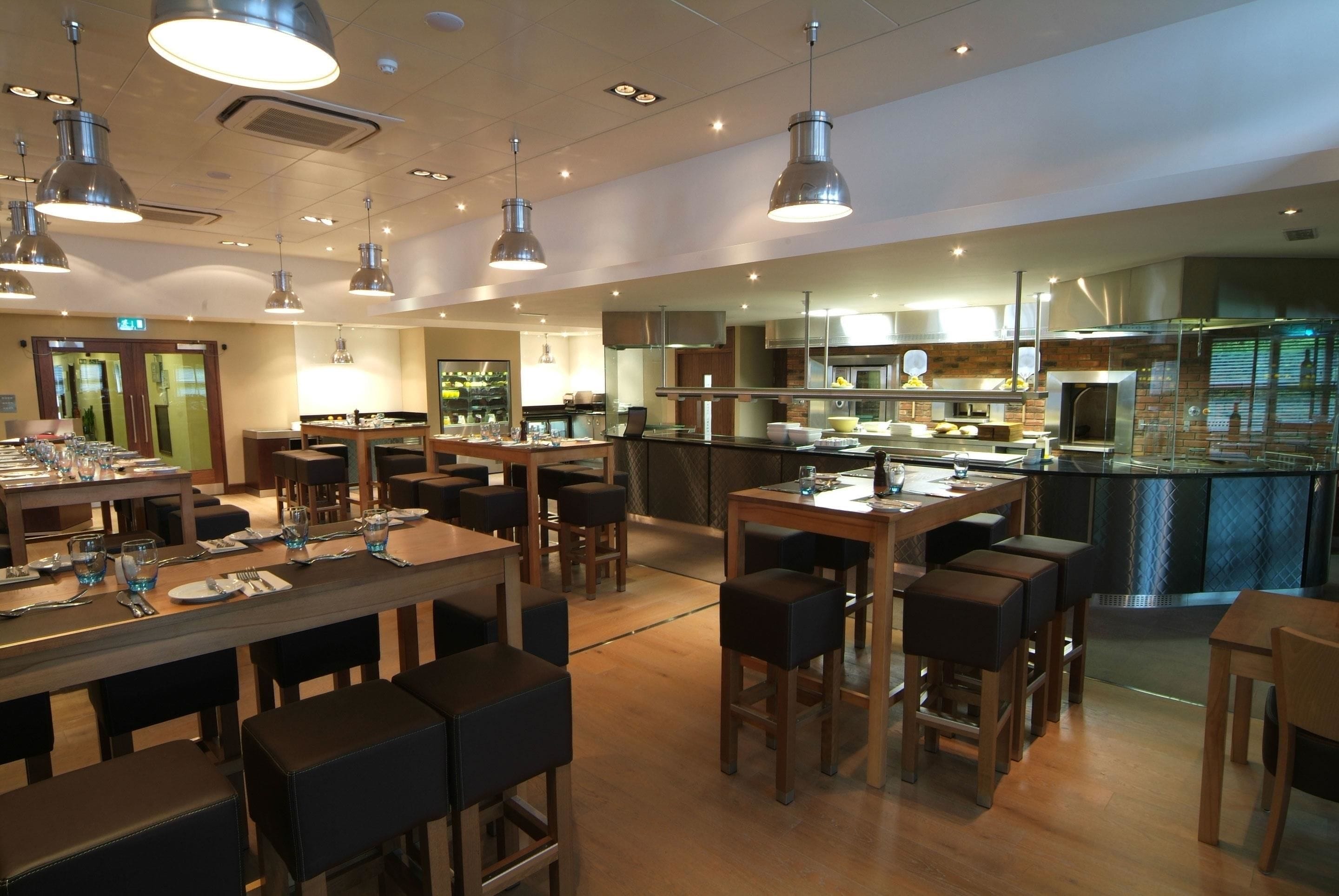 A modern restaurant with multiple dining areas, including a bar and a kitchen visible in the background.