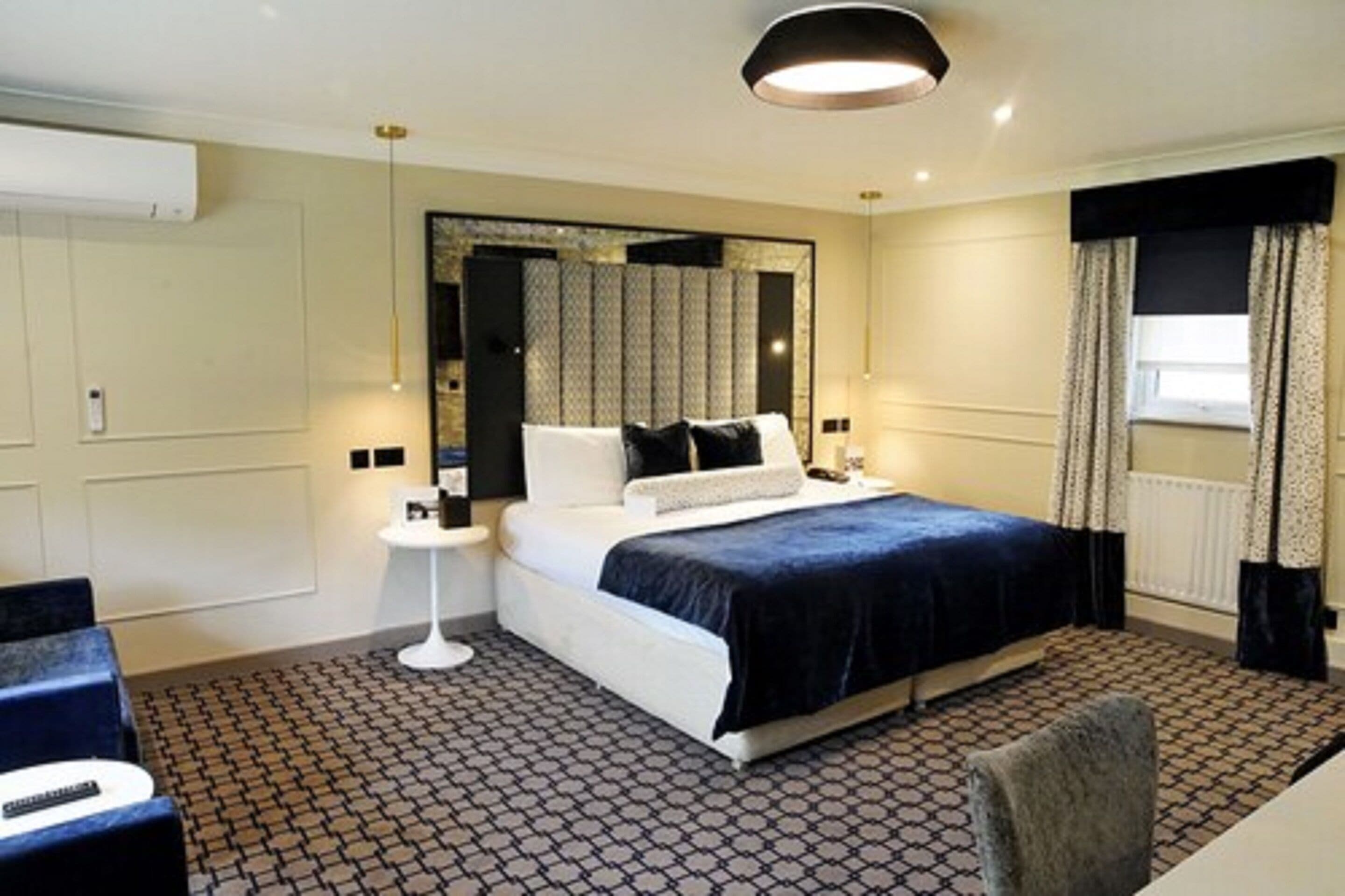 A hotel room with a large bed, a small side table, a chair, and a large mirror.