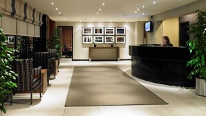 A hotel reception area with a reception desk, framed pictures on the wall, and seating arrangements. - Denham Grove (Uxbridge)