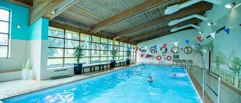 Una piscina interior con vigas de madera, ventanas amplias y equipo de seguridad.