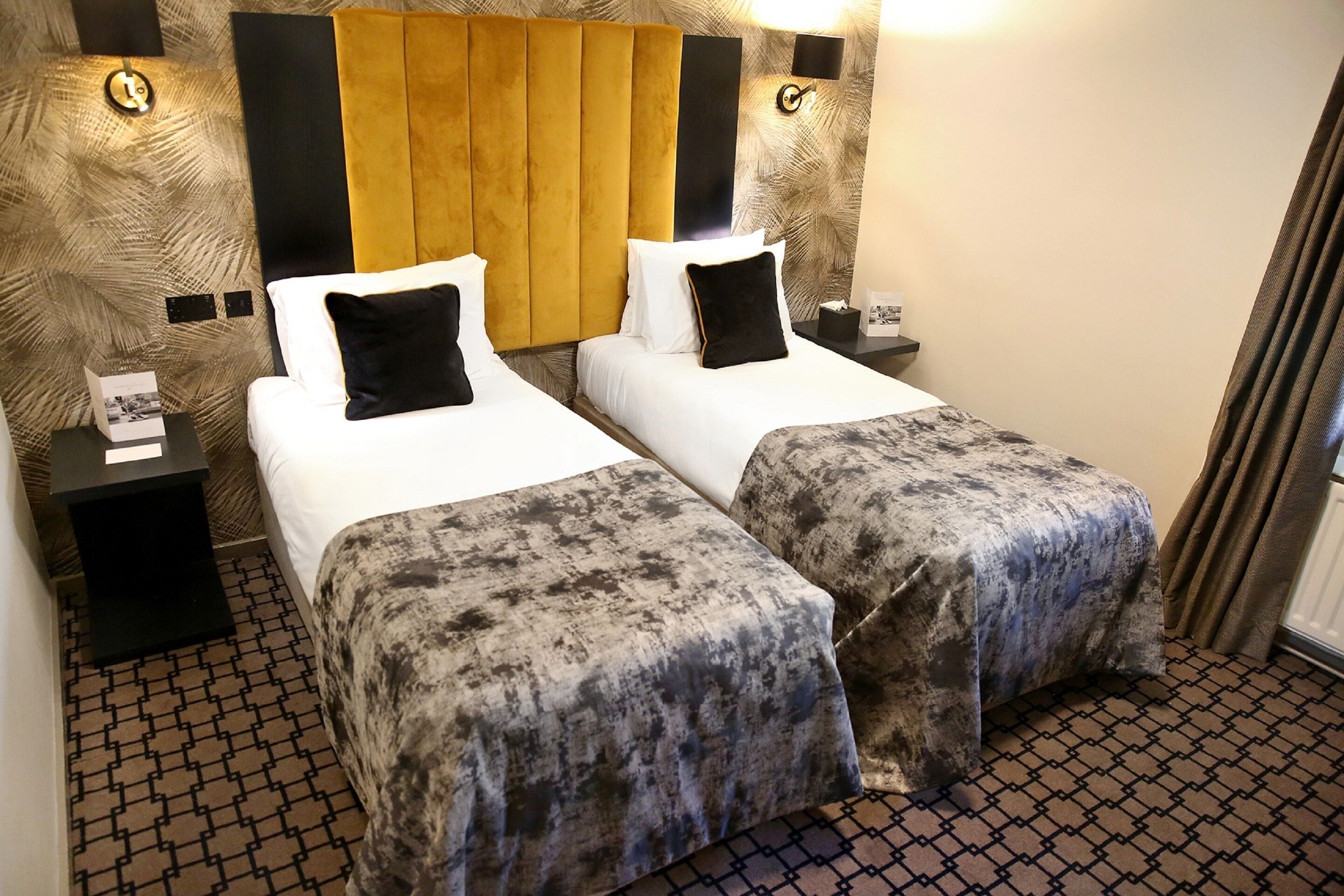 A hotel room with two beds, a patterned carpet, and a headboard with a wooden panel.