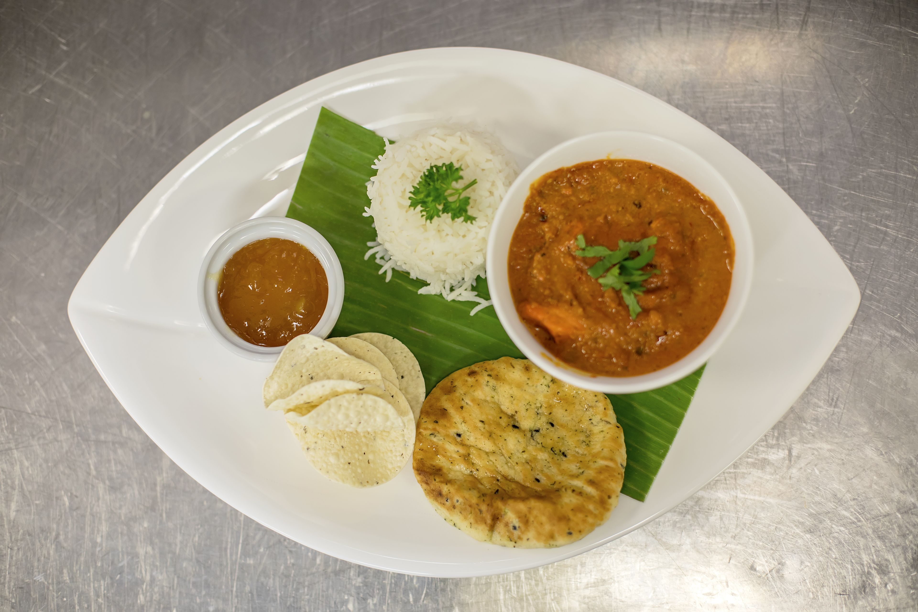 Une assiette de riz blanc, un bol de curry, un petit bol de chutney et deux morceaux de pain plat, le tout servi sur une feuille de bananier.
