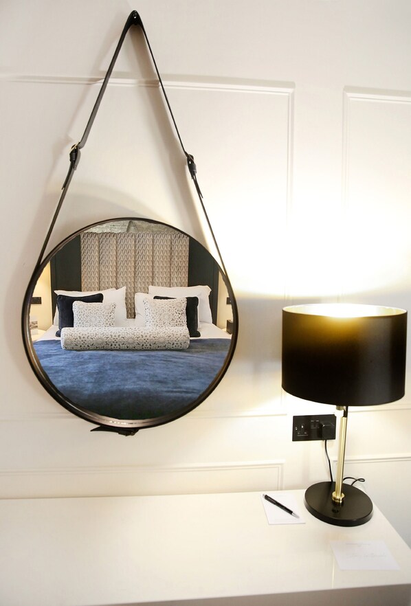 A round mirror with a black frame, a bedside lamp, and a bed with patterned bedding.