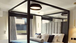A four-poster bed with a headboard, a bedside table, and a view of the outdoors through a window. - Denham Grove (Uxbridge)
