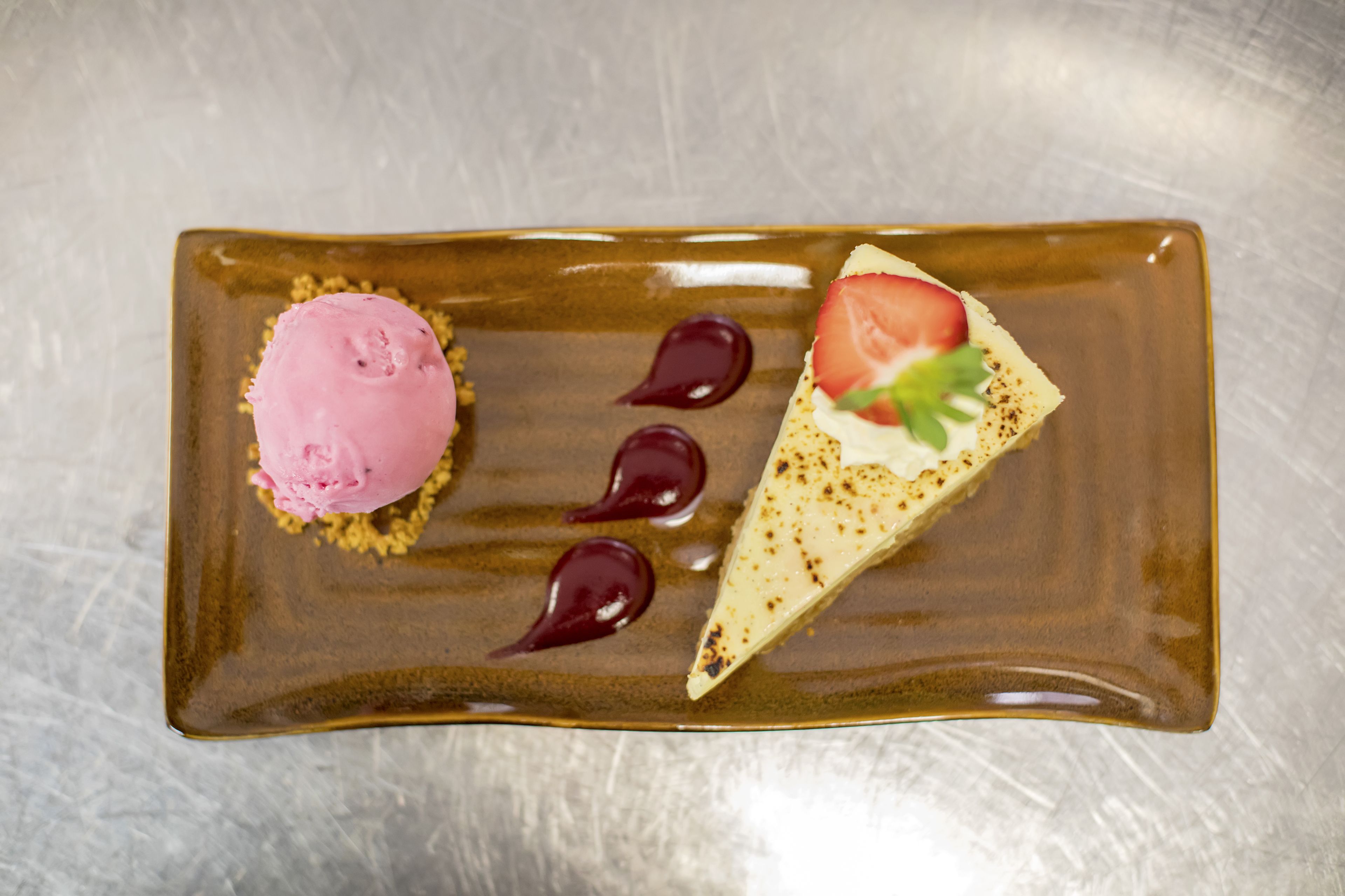 Un plato de postre con helado y una porción de pastel sobre un plato marrón rectangular.