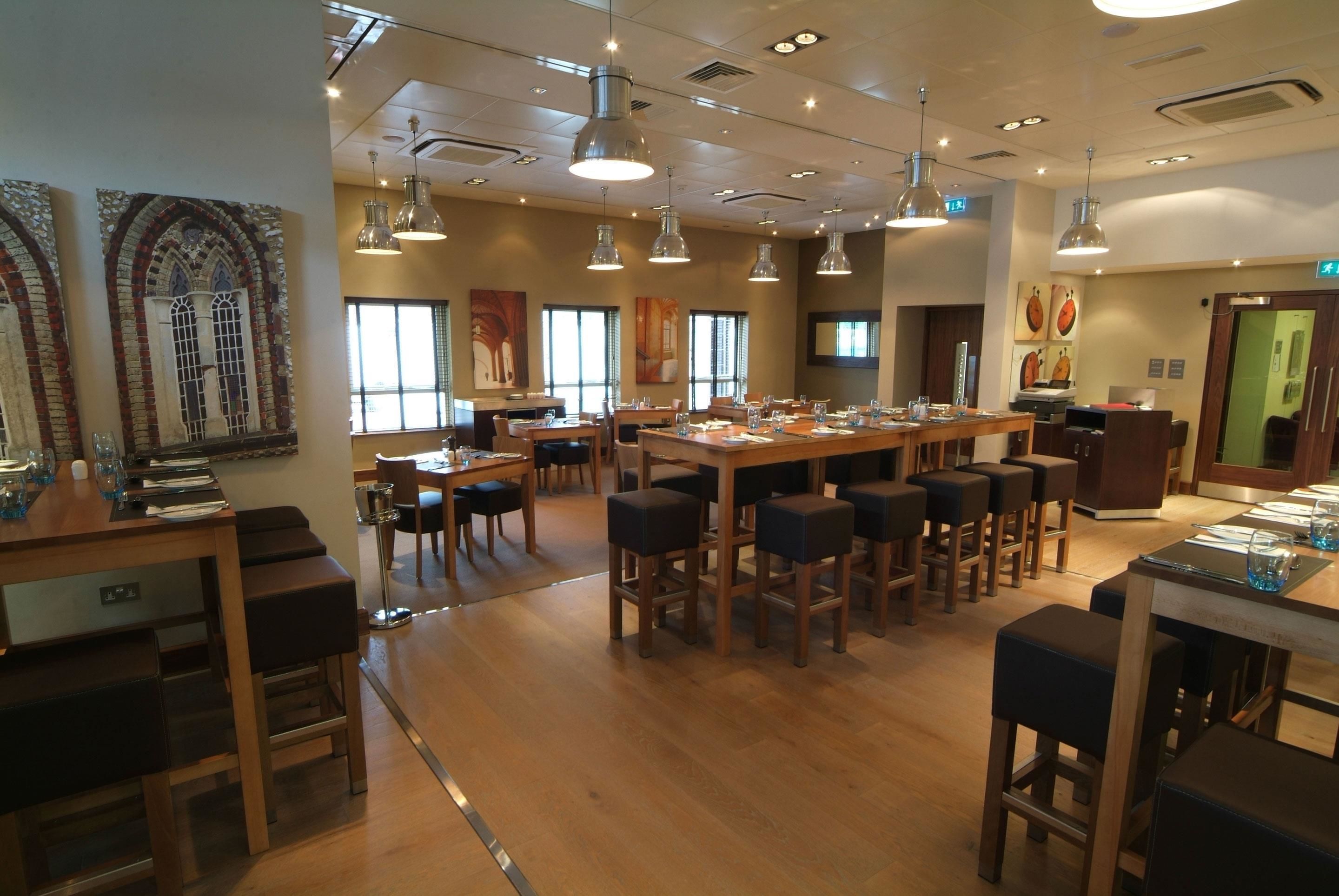 A spacious dining area with multiple tables and chairs, large windows, and hanging pendant lights.