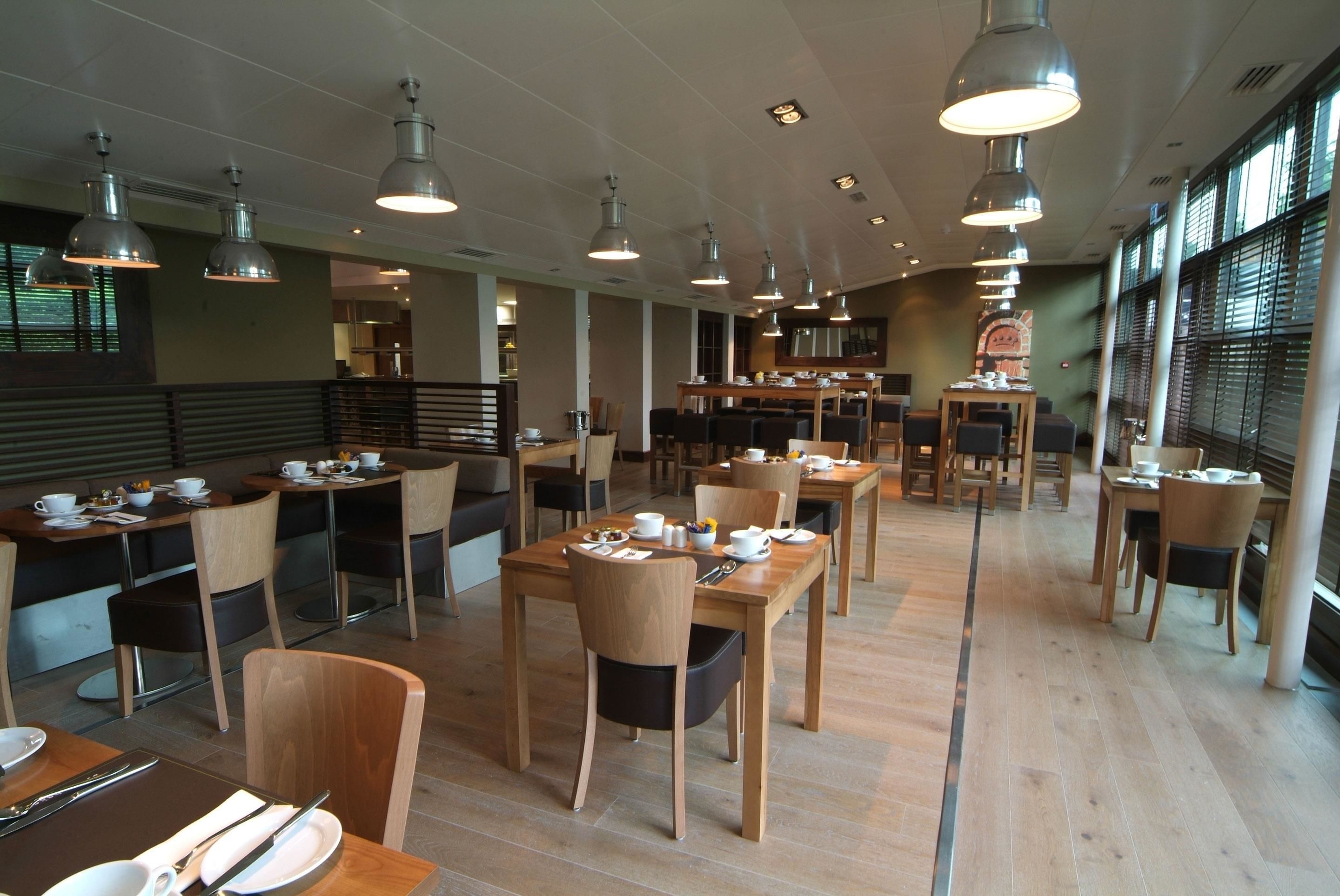 Un'ampia sala ristorante con diversi tavoli e sedie, illuminazione a sospensione e ampie finestre.
