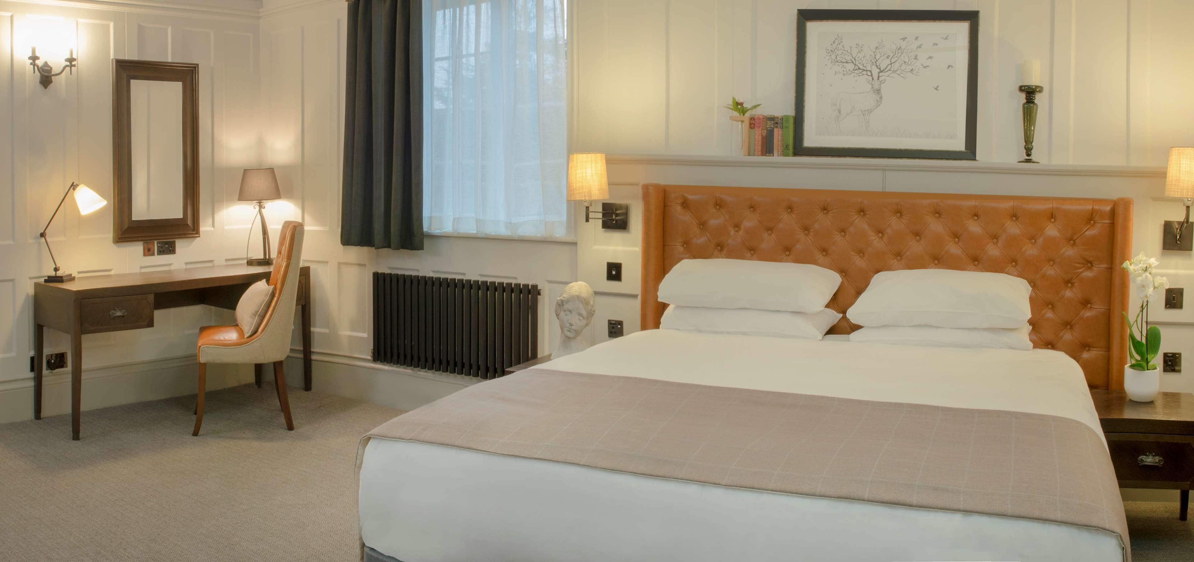 A hotel room with a large bed, a desk with a chair, a radiator, and a window with curtains.