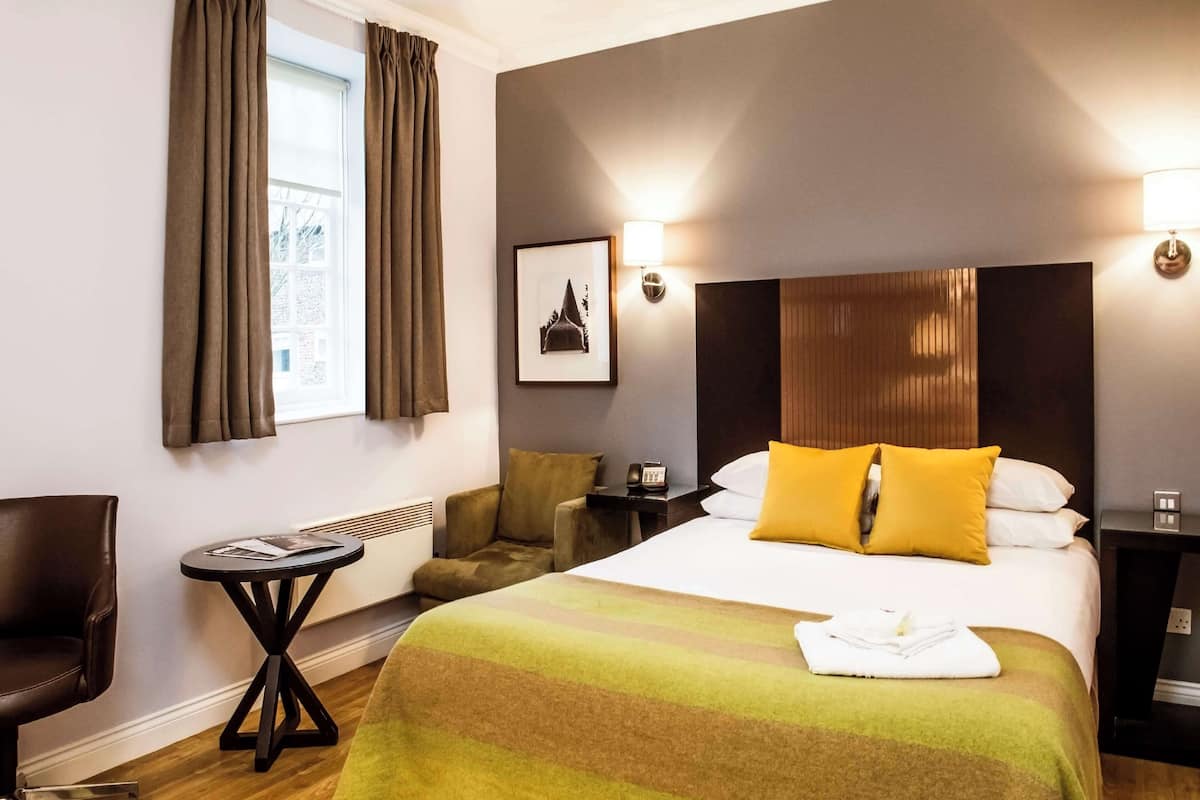 A hotel room with a large bed, a chair, a small table, and a picture on the wall.
