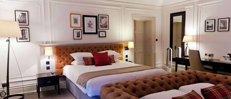 A hotel room with a large bed, a tufted headboard, a desk with a chair, and framed pictures on the walls.
