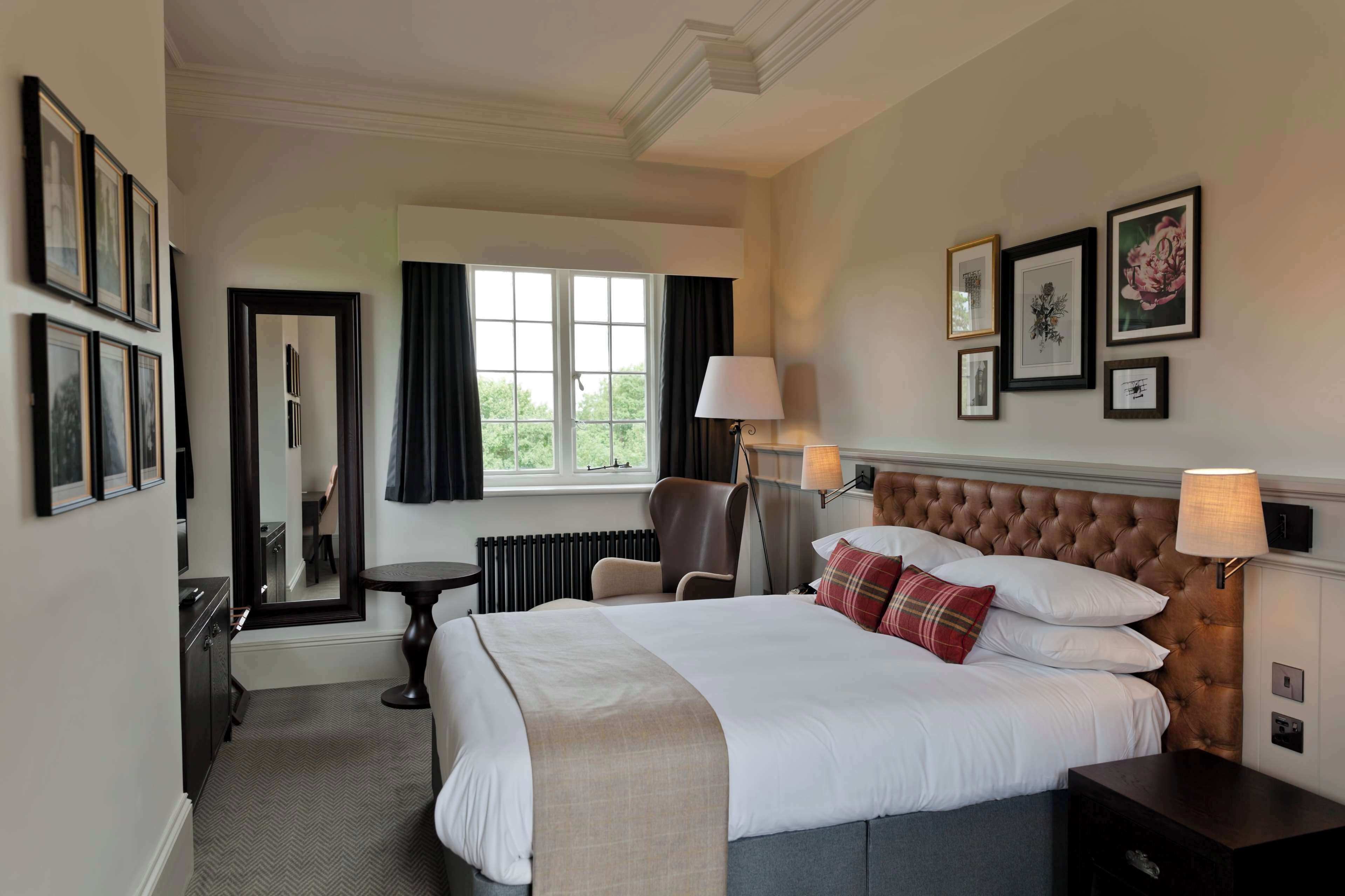 Une chambre d’hôtel avec un grand lit, une chaise, une table, une lampe et des tableaux encadrés au mur.