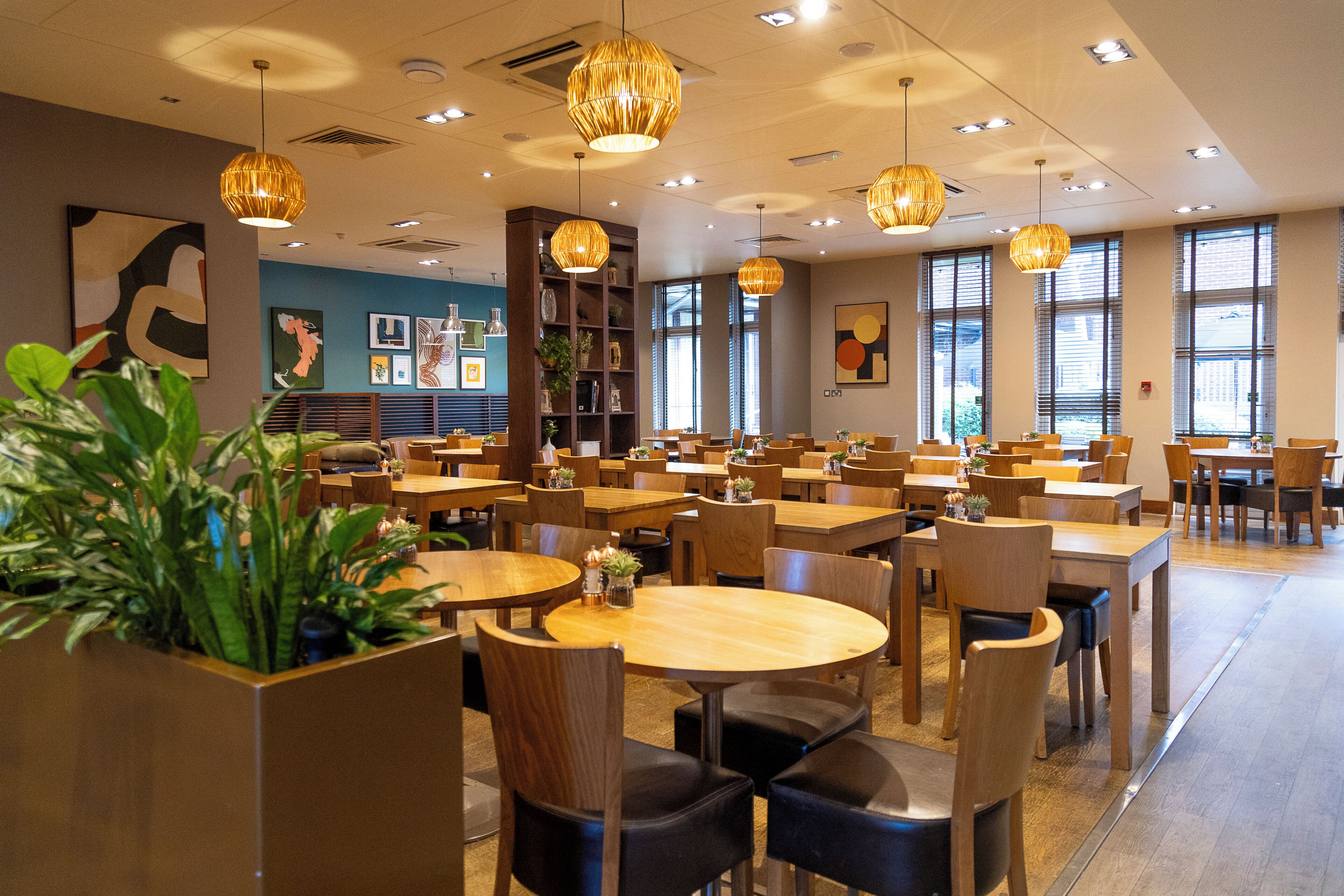 A spacious restaurant with multiple tables and chairs, pendant lighting, and artwork on the walls.