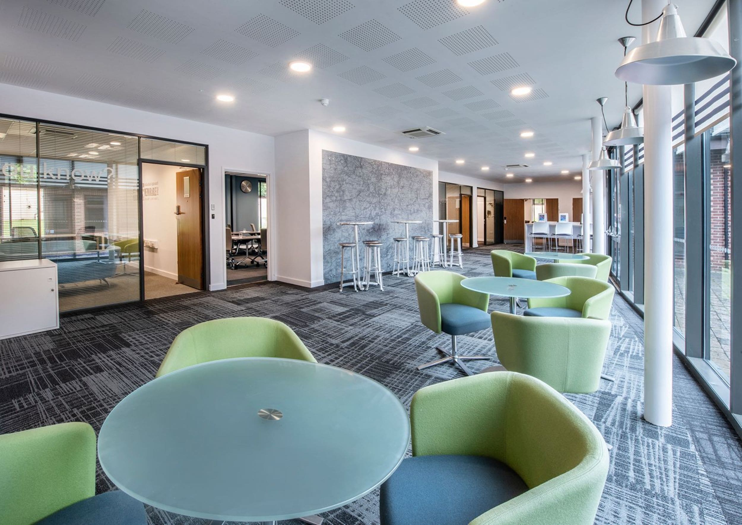 A modern office space with glass partitions, round tables, and green chairs.