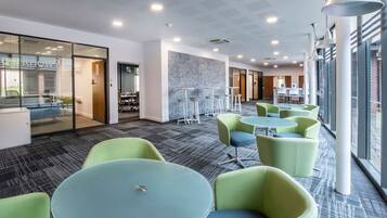 A modern office space with glass partitions, round tables, and green chairs.