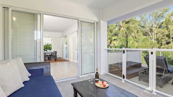 A modern living room with a sofa, a wooden coffee table with a bottle and glasses, and a balcony with wicker furniture.