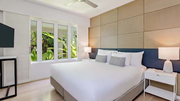A modern bedroom with a large bed, a ceiling fan, a nightstand, and a window with a view of greenery.