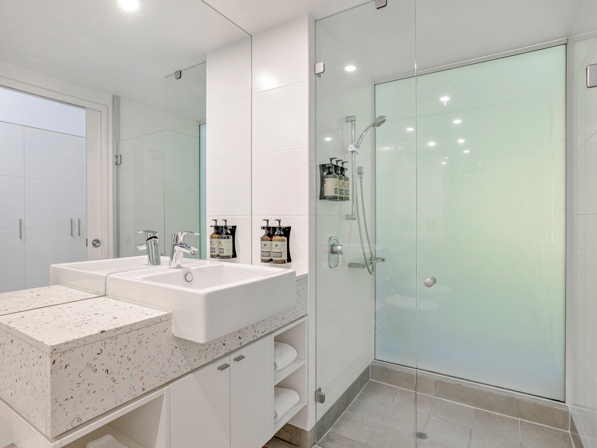 A modern bathroom with a double sink vanity, a glass shower enclosure, and a large mirror.