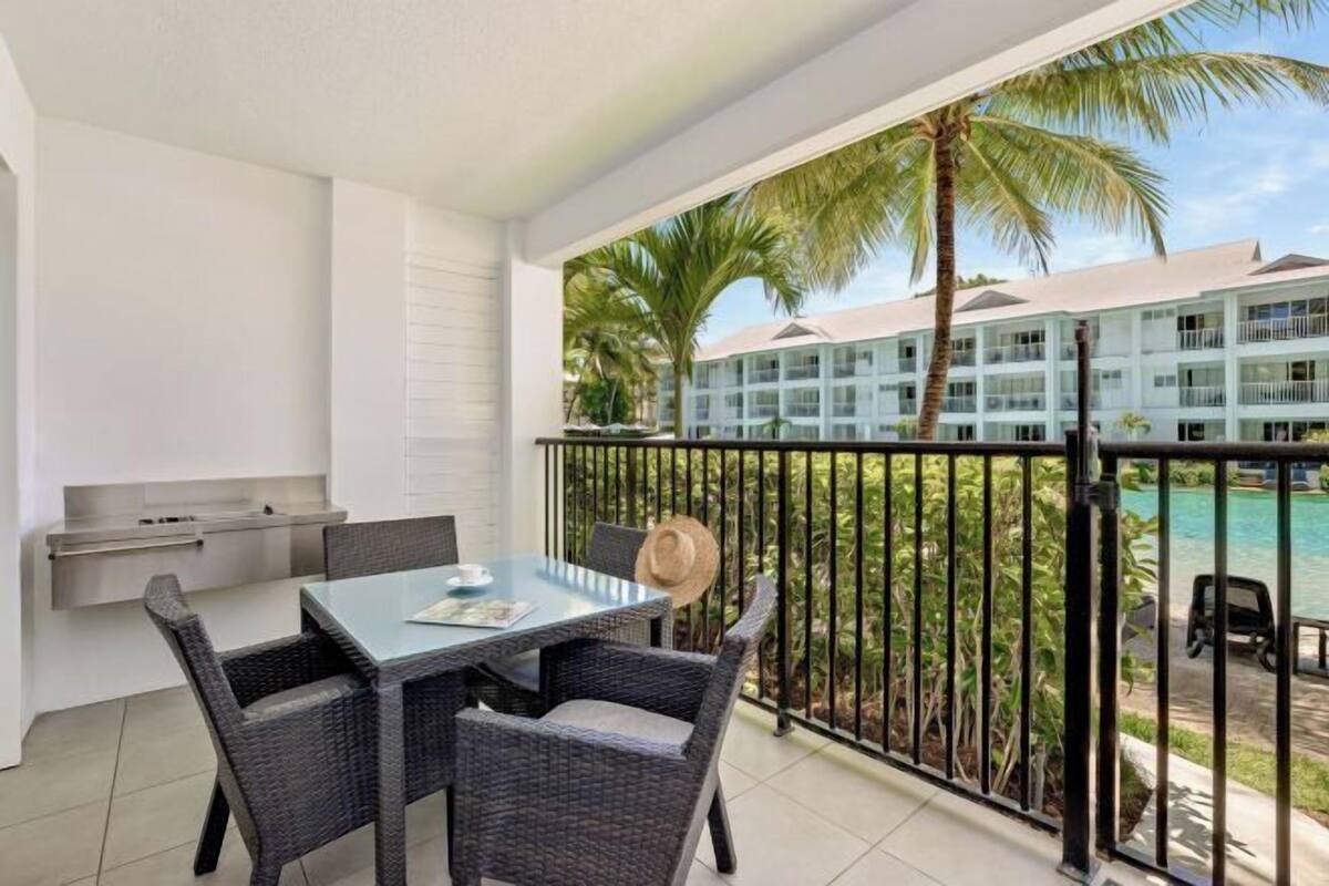 A balcony with a dining table and chairs, a hat, and a view of a pool and hotel building.