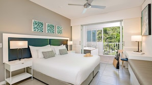 A modern hotel room with a large bed, a ceiling fan, a balcony with a view of greenery, and a desk with a chair. - Peppers Beach Club (Port Douglas)
