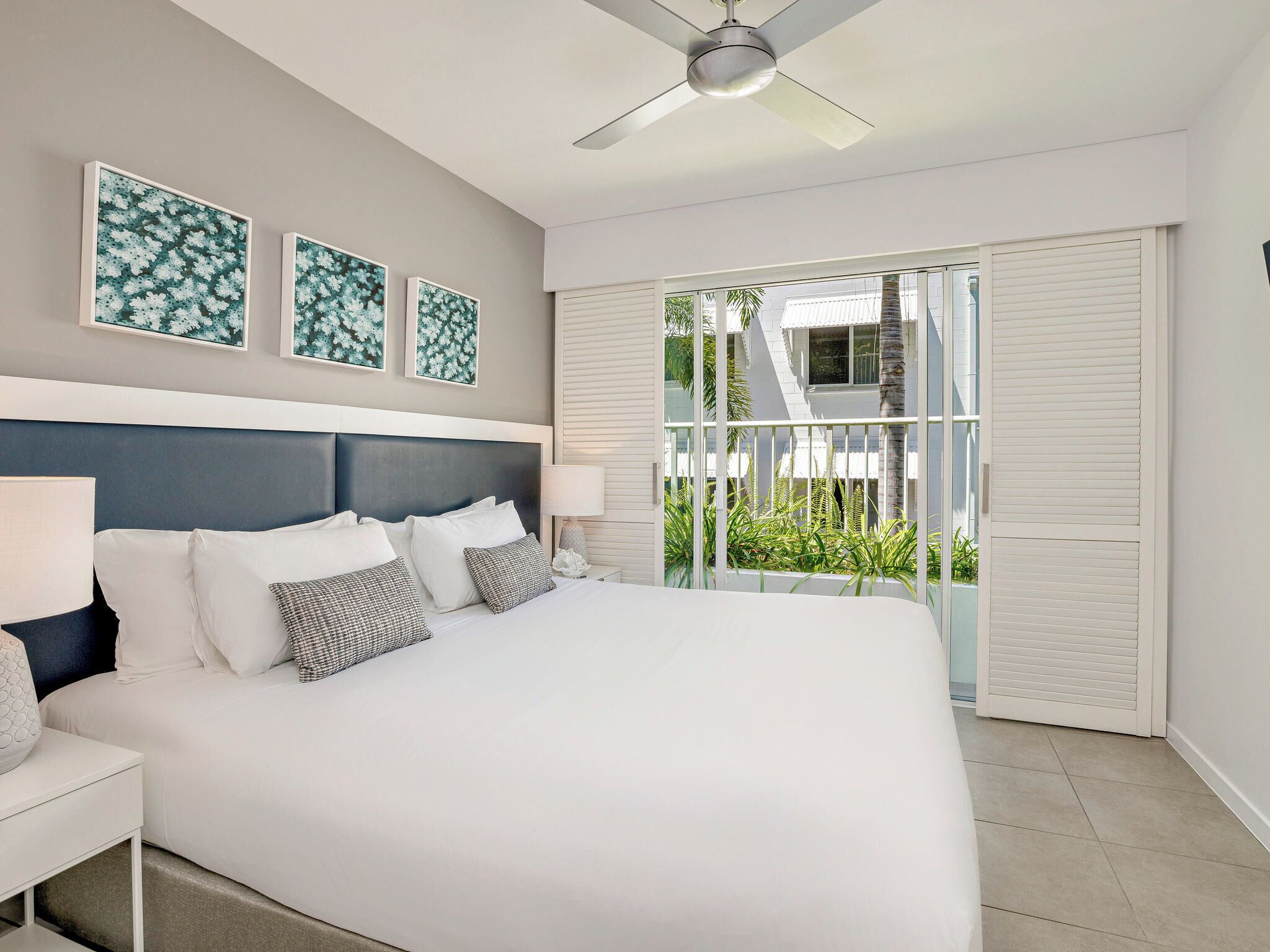 A modern bedroom with a large bed, a ceiling fan, and a view of the outdoors through a sliding glass door.