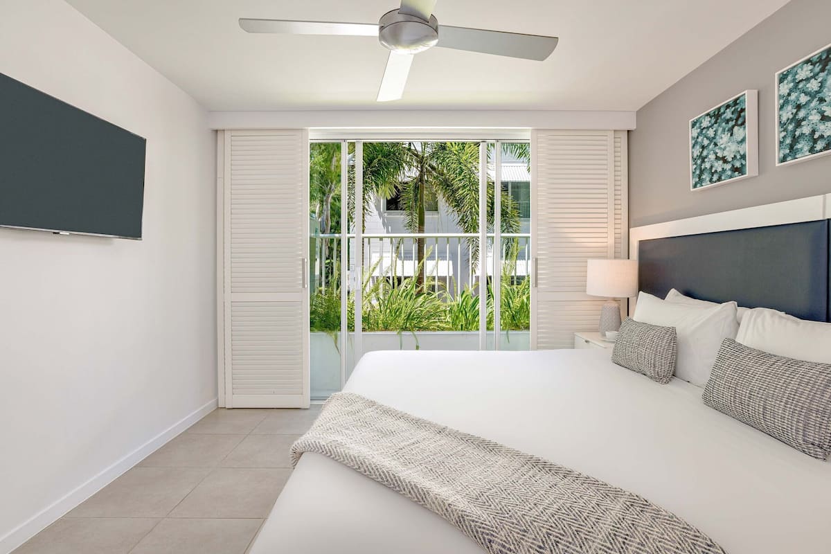 A modern hotel room with a large bed, ceiling fan, and a view of palm trees through the sliding glass door.