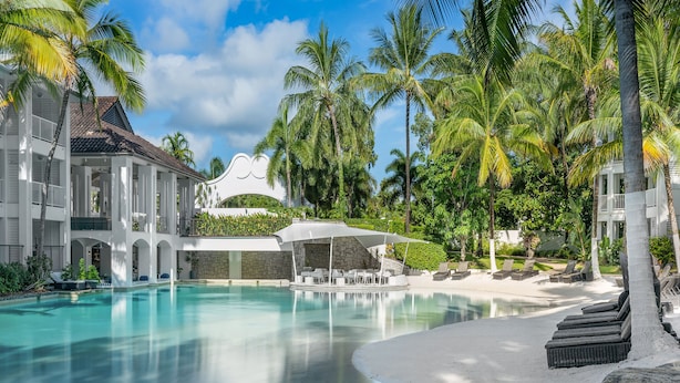A resort with a swimming pool, palm trees, and a covered seating area. - Peppers Beach Club (Port Douglas)